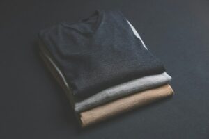 Man examining wool, linen, cotton, and cashmere fabric swatches beside tailored clothing.