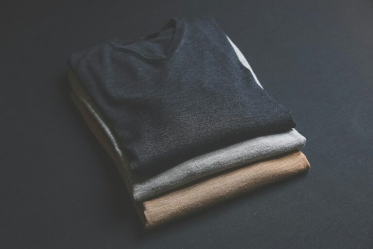 Man examining wool, linen, cotton, and cashmere fabric swatches beside tailored clothing.