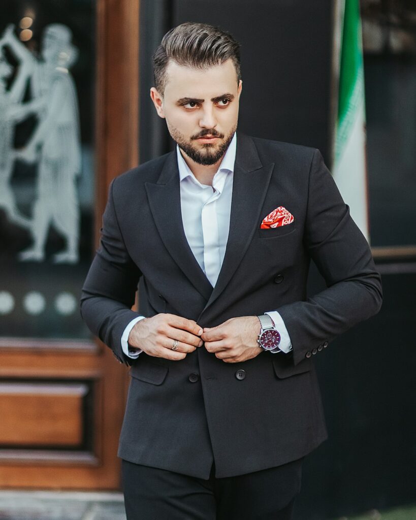 Man examining the fit of a tailored jacket and trousers in front of a full-length mirror.