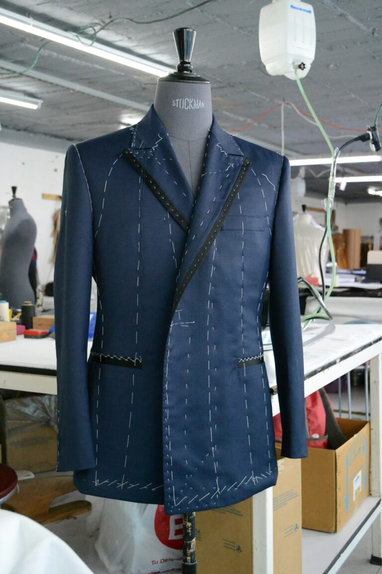 A tailor measures a man's jacket while fabric swatches and a partially finished suit rest nearby.